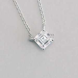 May include: A silver necklace with a square, clear gemstone pendant. The pendant is set in a square shape with multiple facets, reflecting light. The chain is delicate and silver. The text "VEXA JEWEL" is visible.