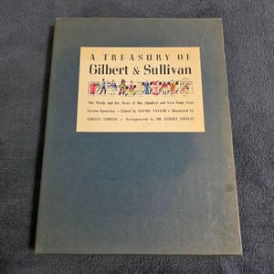 May include: A blue hardcover book titled A Treasury of Gilbert & Sullivan. The cover features a cream-colored label with the title, a musical staff with small colorful character illustrations, and text listing the editor, illustrator, and arranger.