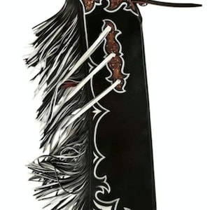 以下が含まれることがあります： 白の装飾トリムとフリンジが付いた黒革のチャップス。チャップスは、茶色のツールレザーのアクセントと白い革のネクタイが特徴です。チャップスは乗馬用に設計されており、ウエスタンスタイルです。