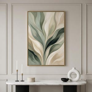 Op de afbeelding: Abstracte botanische kunstprint in een gouden lijst. Het kunstwerk toont vloeiende, gelaagde bladeren in tinten groen, beige en crème. De schildering wordt tentoongesteld boven een console met marmeren blad en decoratieve items.