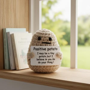 May include: A crocheted potato figure with black button eyes and a stitched mouth. It holds a sign that reads "Positive potato. I may be a tiny potato, but I believe in you. Go do your thing!" The figure is light brown.