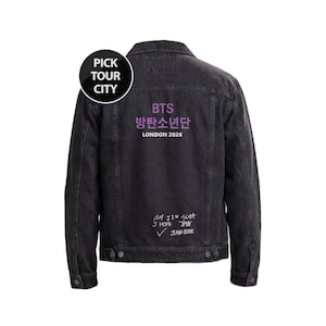 Pode incluir: Jaqueta jeans preta com o texto "BTS 방탄소년단 LONDON 2026" em roxo. A parte de trás da jaqueta também apresenta nomes manuscritos e uma marca de seleção. Um logotipo circular "PICK TOUR CITY" está no canto superior esquerdo.