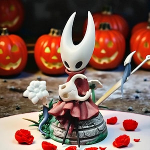May include: A detailed figurine of a character with a white head and a red cloak, standing on a stone base with green accents. The background features carved orange pumpkins, and red rose petals are scattered around the base.
