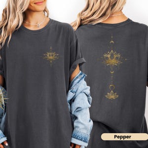 May include: Dark gray t-shirt with a gold lotus flower design on the front and back. The back design includes a lotus flower, crescent moons, and a vertical line of dots. The word "Pepper" is at the bottom.