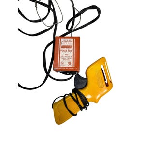May include: An orange Aurora Power Pack with black wires and a yellow controller. The power pack has text that reads "Aurora Power Pack" and "13.5 V. DC". The yellow controller has the word "Aurora" printed on it.