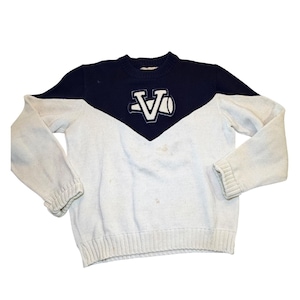 May include: A vintage, two-tone sweater in white and navy blue. The sweater features a navy blue yoke with a white embroidered "VA" logo. The sleeves and lower body are white. The sweater has ribbed cuffs and hem.