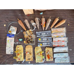May include: A collection of vintage fishing tackle, including cork floats, packaged lures, and spools of wire. The items are arranged on a dark wooden surface, with various colors and textures visible. Some packages have text, and the overall theme is angling.