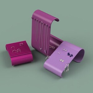 May include: A set of three magenta jewelry organizers. One is a rectangular earring holder, another is a necklace holder, and the third is a curved earring holder. The organizers are on a muted green background.