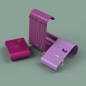 Op de afbeelding: Een set van drie magenta sieraden organizers. Eén is een rechthoekige oorbelhouder, een andere is een kettinghouder en de derde is een gebogen oorbelhouder. De organizers staan op een gedempte groene achtergrond.