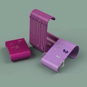 May include: A set of three magenta jewelry organizers. One is a rectangular earring holder, another is a necklace holder, and the third is a curved earring holder. The organizers are on a muted green background.