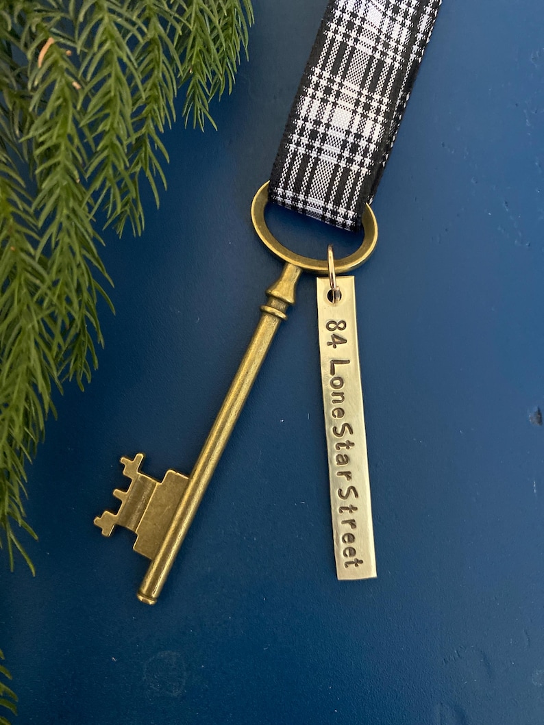 May include: A gold-toned skeleton key with a tag attached that reads "84 LoneStar Street". The key is attached to a black and white plaid ribbon.