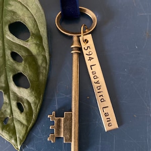 May include: A gold-toned skeleton key with a decorative keyhole and a tag attached. The tag is engraved with the text "594 Ladybird Lane".