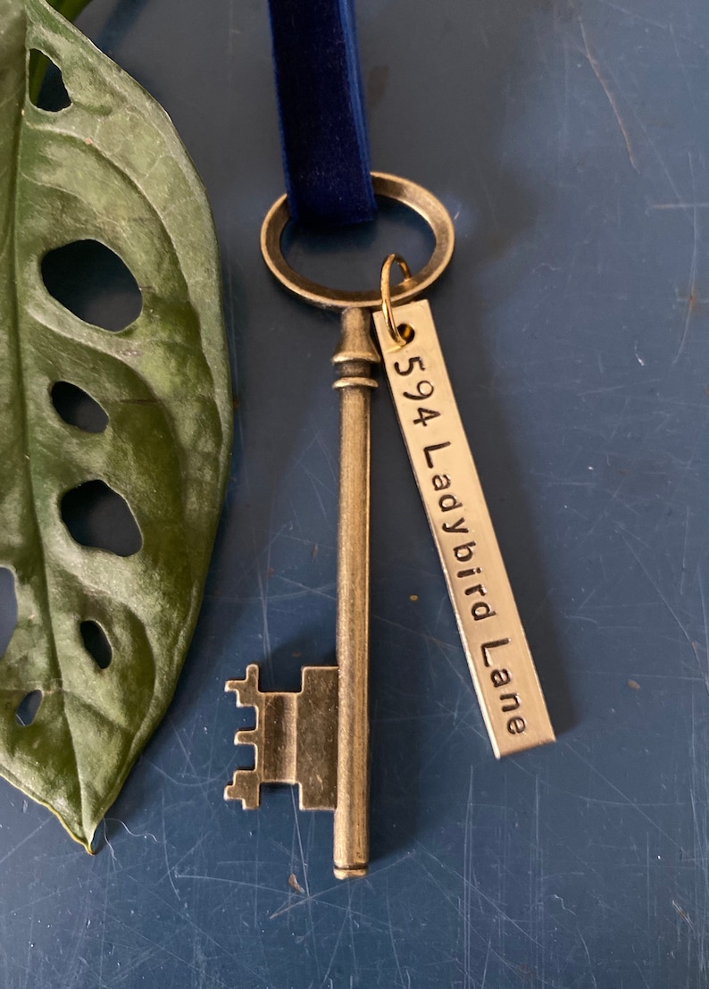 May include: A gold-toned skeleton key with a decorative keyhole and a tag attached. The tag is engraved with the text "594 Ladybird Lane".