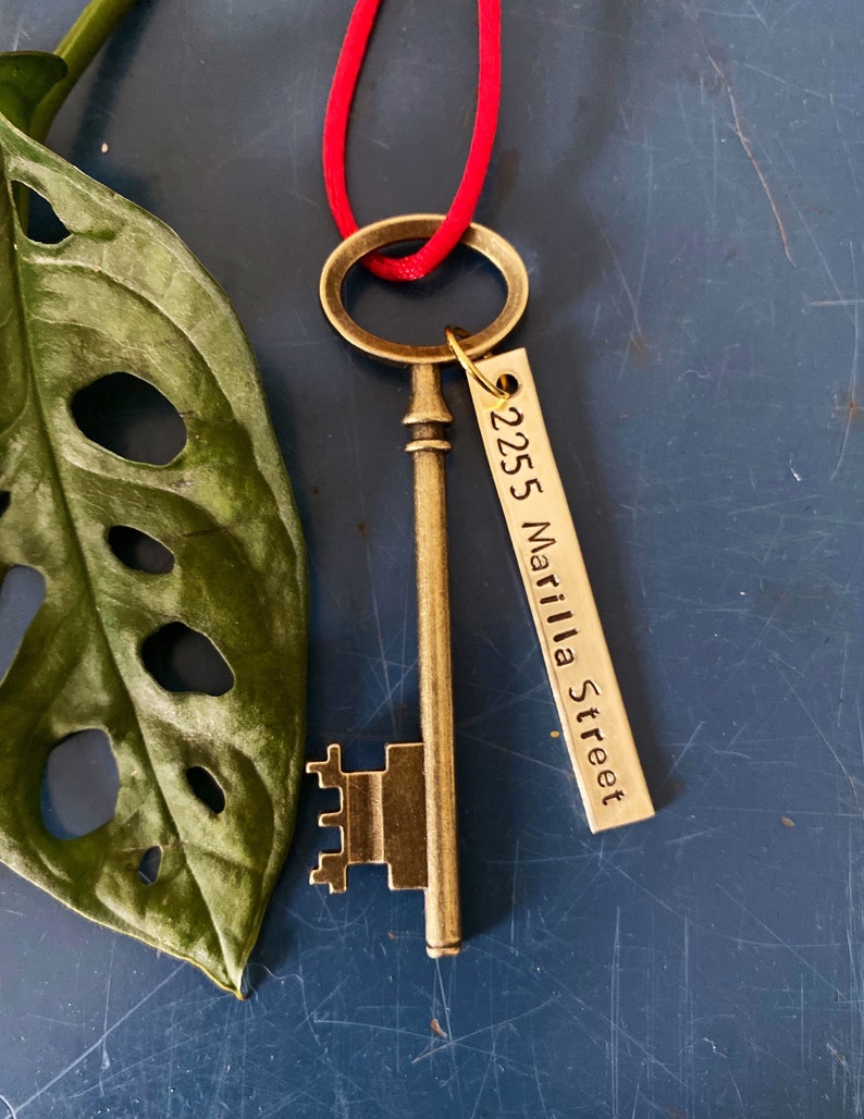 May include: A gold-toned skeleton key with a decorative keyhole and a tag that reads "2255 Matilla Street" hanging from a red cord.