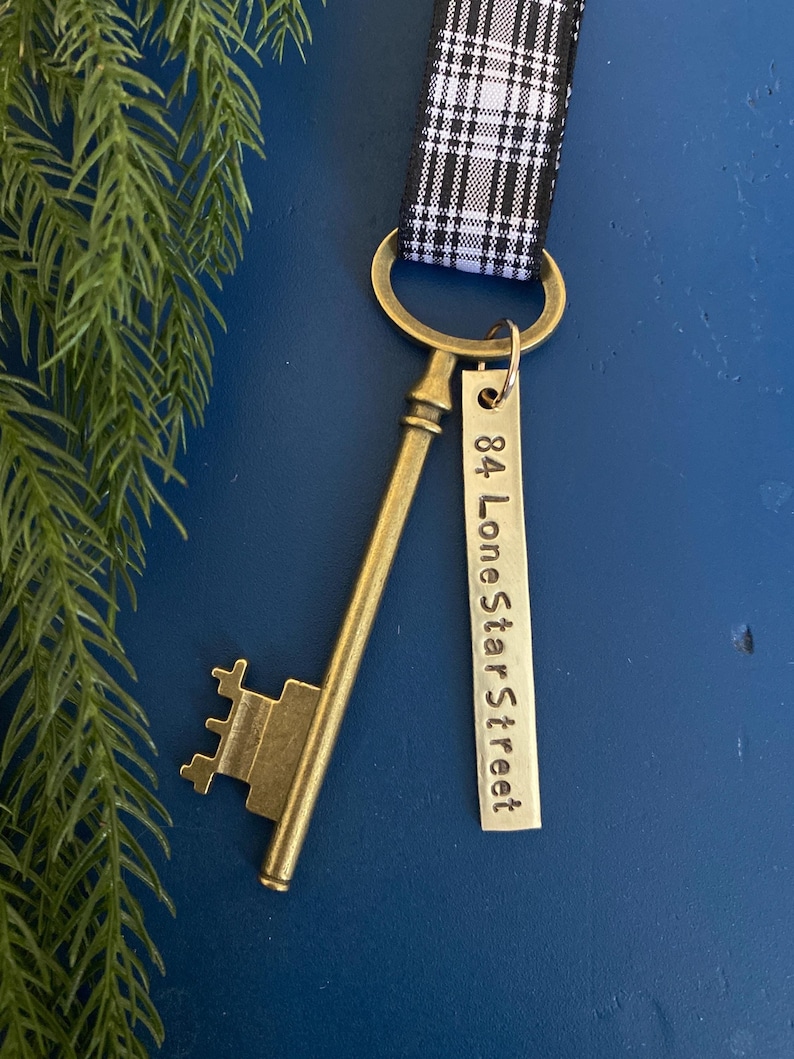 antiqued brass key with hand stamped custom address tag and plaid ribbon in black and white used as a housewarming gift or tree decoration