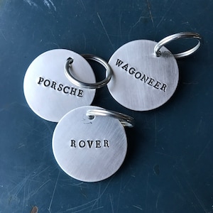 May include: Three silver keyrings with round metal tags. The tags are engraved with the words "Porsche", "Wagoneer", and "Rover".