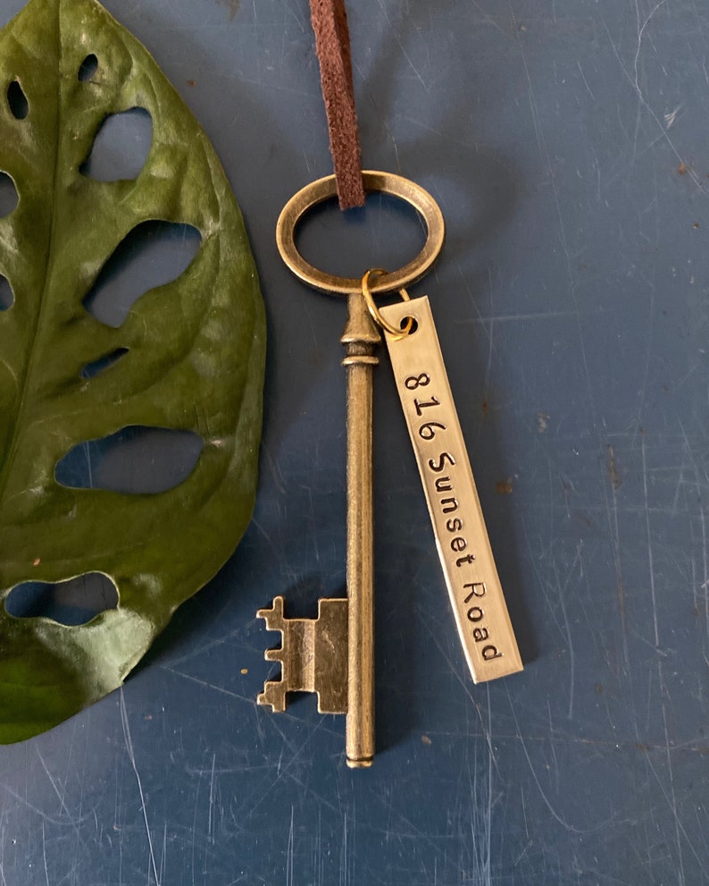 May include: A gold-toned skeleton key with a brown leather cord and a metal tag that reads "816 Sunset Road".