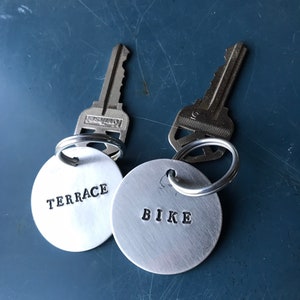 May include: Two silver keyrings with round metal tags. The tag on the left says "TERRACE" and the tag on the right says "BIKE".