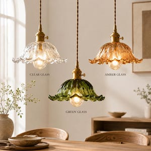 Può includere: Tre lampade a sospensione con finiture in ottone e paralumi in vetro smerlato trasparente, ambra e verde. Ogni lampada è appesa a un cavo intrecciato. Le etichette indicano CLEAR GLASS, AMBER GLASS e GREEN GLASS per ogni apparecchio.
