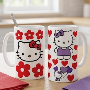 May include: Two white ceramic mugs with Hello Kitty designs. One mug features Hello Kitty with red flowers, the other with red hearts and Hello Kitty holding balloons. A spoon rests in one mug. Red and purple napkins are on the table.