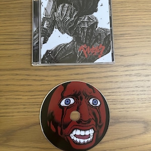May include: A CD case with a black and white illustration of a character in armour, with Japanese text. Below, a CD with a red face design with blue eyes and an open mouth.