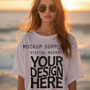 May include: A white t-shirt with the text "YOUR DESIGN HERE" in bold black letters. The shirt also has the text "MOCKUP SUPPLY CO. DIGITAL MOCKUPS". The person is wearing aviator sunglasses.