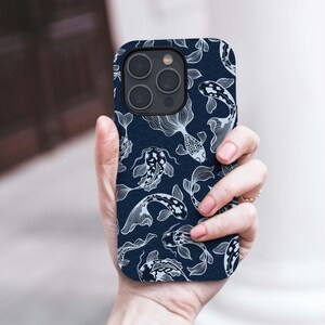 May include: A navy blue phone case featuring a repeating pattern of white koi fish. The design includes detailed outlines of the fish and wave-like patterns, creating a flowing, aquatic theme. The case has a glossy finish and a camera cutout.