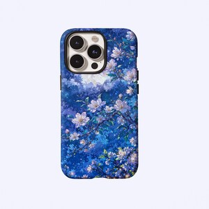 Puede incluir: Una funda para smartphone con un fondo de cielo nocturno azul vibrante, una luna llena y ramas de cerezo en flor blancas dispersas. El diseño incluye patrones florales detallados con pétalos de color rosa claro y blanco sobre un fondo estrellado.