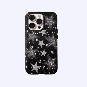 Könnte beinhalten: Schwarze Handyhülle mit Sternenmuster. Die Hülle hat ein sich wiederholendes Design aus silbernen Glitzersternen mit braunen Umrissen und kleineren weißen Sternen. Die Hülle ist für ein Smartphone konzipiert.