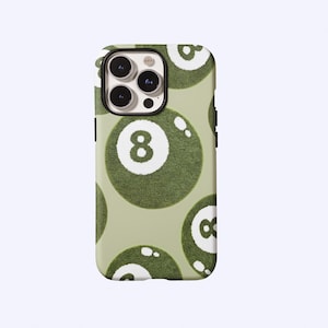 May include: A phone case featuring a repeating pattern of green eight balls on a light green background. The eight balls have a textured appearance and white number 8s. The phone case has a black border around the camera.