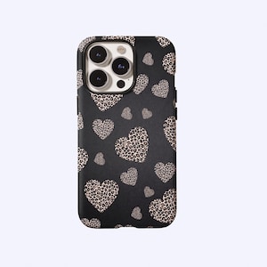 May include: Black phone case with a leopard print heart pattern. The case has a matte finish and features multiple heart shapes in varying sizes. The leopard print is a mix of tan and brown spots on a cream background.