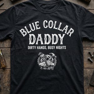 Puede incluir: Camiseta negra con las palabras "BLUE COLLAR DADDY" en blanco, sobre el texto "DIRTY HANDS, BUSY NIGHTS". Un gráfico de herramientas cruzadas está debajo del texto. La camiseta tiene una etiqueta que dice "BLUE COLLAR APPAREL".