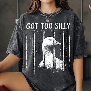 May include: Dark gray t-shirt with the text "GOT TOO SILLY" above a white graphic of a goose. The goose is behind white vertical lines. The shirt has a vintage, washed look.