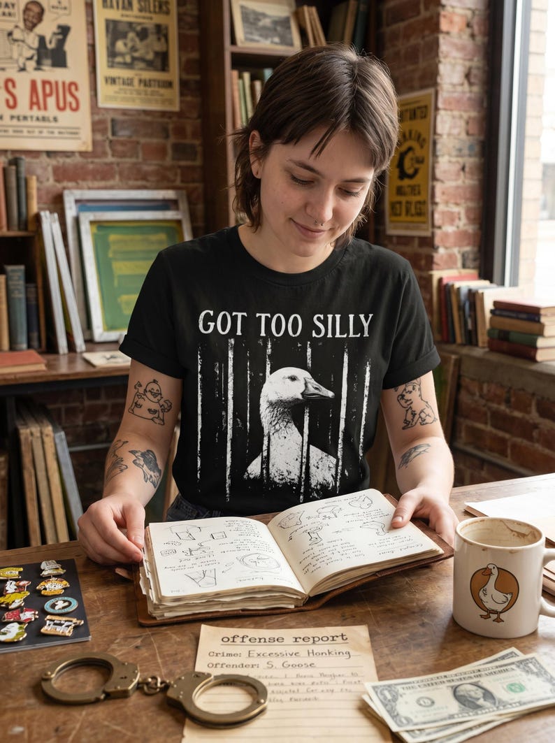 May include: Black t-shirt with the text "GOT TOO SILLY" and a graphic of a goose behind bars. The image includes a mug with a goose design, a notebook, handcuffs, and a dollar bill.