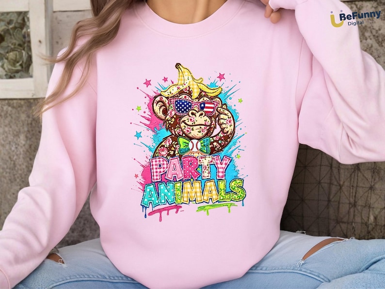 Puede incluir: Sudadera rosa claro con un mono de dibujos animados con gafas de sol con un dise&ntilde;o de bandera estadounidense y una c&aacute;scara de pl&aacute;tano en la cabeza. Las palabras "PARTY ANIMALS" se muestran en letras de estilo graffiti coloridas.