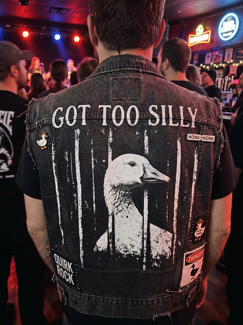 May include: A black denim vest with a large white graphic of a goose behind bars. The text "GOT TOO SILLY" is above the goose. Patches and pins with duck imagery and the words "HONK HONK" and "QUIRK ROCK" are also visible.