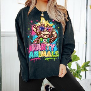 Puede incluir: Sudadera negra de cuello redondo con un gr&aacute;fico colorido de un mono con gafas de sol y pajarita. El mono tiene un pl&aacute;tano en la cabeza. Las palabras "PARTY ANIMALS" est&aacute;n escritas en estilo graffiti.