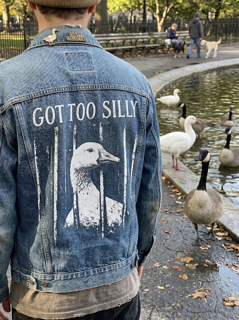 May include: A denim jacket with a goose graphic and the text "GOT TOO SILLY" in white. The jacket has a small goose pin on the collar. Geese are visible in the background near a pond.