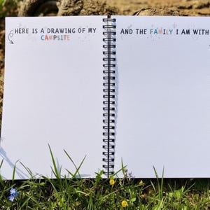 Puede incluir: Cuaderno espiral abierto con p&aacute;ginas blancas en blanco, sobre hierba. El texto "HERE IS A DRAWING OF MY CAMPSITE" y "AND THE FAMILY I AM WITH" est&aacute; impreso en la parte superior de las p&aacute;ginas. El cuaderno est&aacute; abierto, listo para dibujar o escribir.