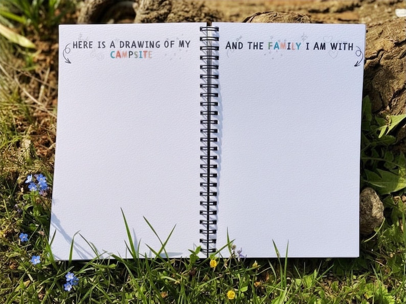 Puede incluir: Cuaderno espiral abierto con p&aacute;ginas blancas en blanco, sobre hierba. El texto "HERE IS A DRAWING OF MY CAMPSITE" y "AND THE FAMILY I AM WITH" est&aacute; impreso en la parte superior de las p&aacute;ginas. El cuaderno est&aacute; abierto, listo para dibujar o escribir.