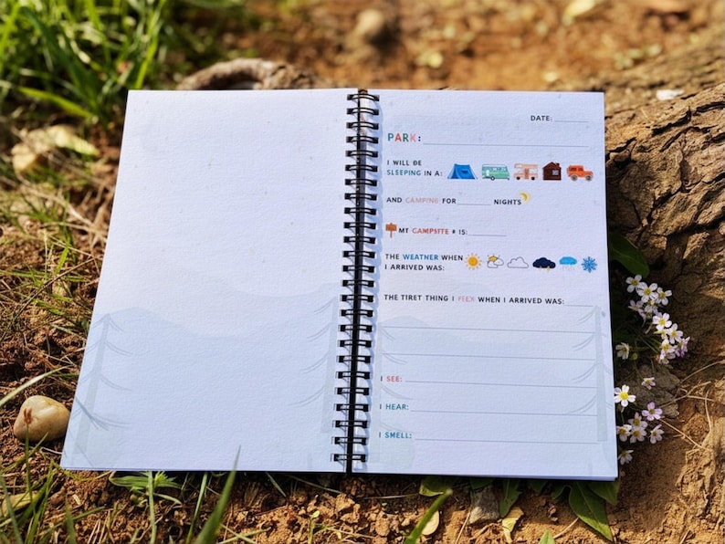 Puede incluir: Diario de camping con espiral abierto, con p&aacute;ginas rayadas y elementos decorativos. La p&aacute;gina izquierda est&aacute; en blanco, mientras que la p&aacute;gina derecha presenta indicaciones para registrar experiencias de camping. El diario est&aacute; abierto sobre una superficie natural.