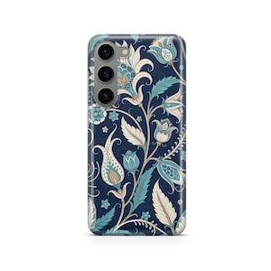 May include: A navy blue phone case featuring a detailed floral pattern in shades of blue, cream, and gold. The design includes stylized flowers, leaves, and vines, creating a vintage aesthetic. The case has a camera module with three lenses.