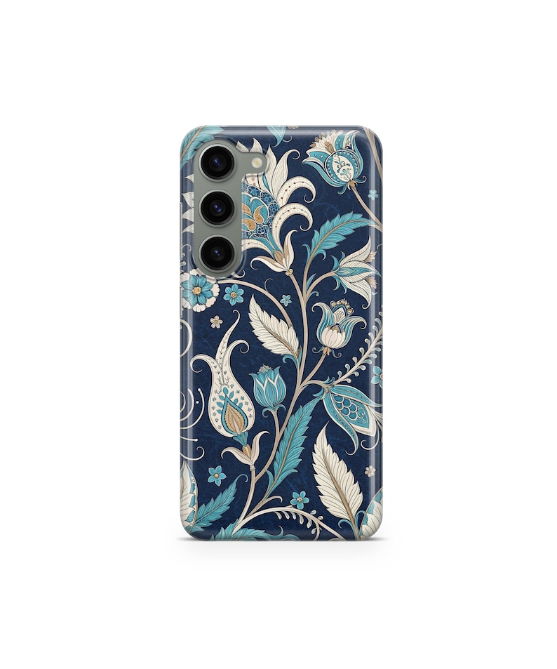 May include: A navy blue phone case featuring a detailed floral pattern in shades of blue, cream, and gold. The design includes stylized flowers, leaves, and vines, creating a vintage aesthetic. The case has a camera module with three lenses.