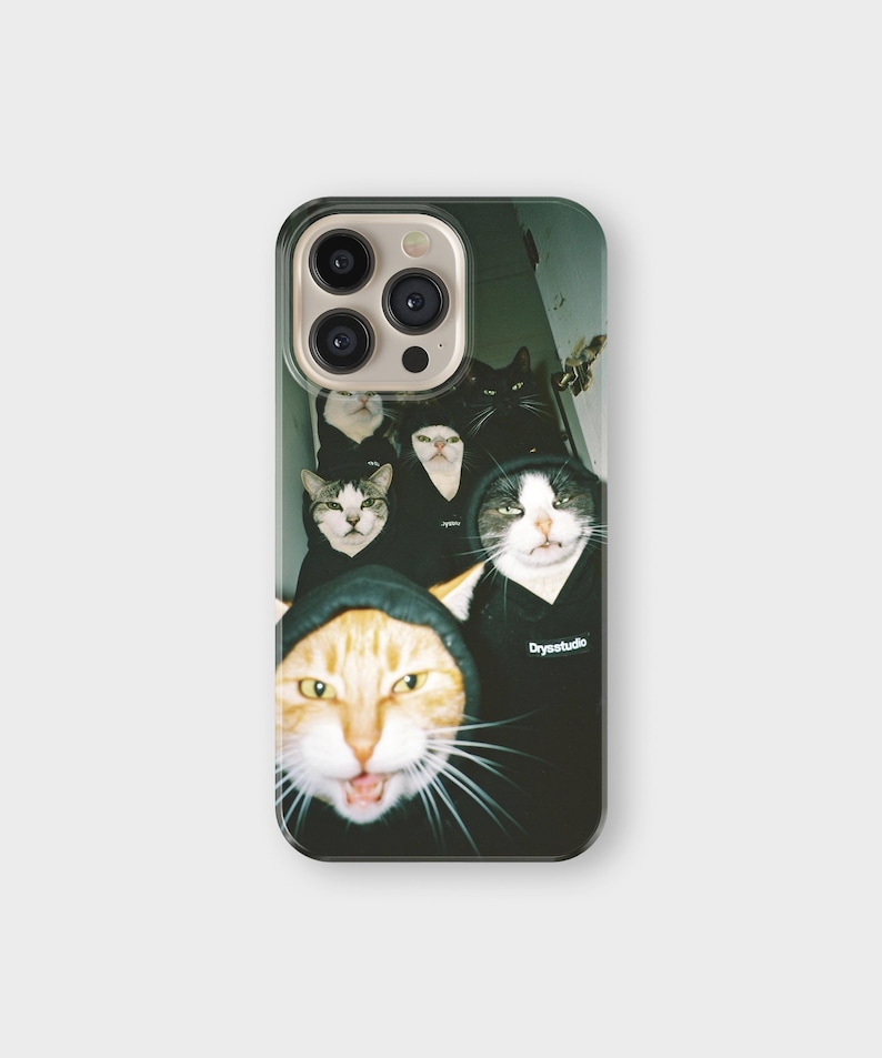 May include: A phone case featuring a group of cats wearing black hoodies. The cats have various fur patterns, including orange, black, and white. The text "Drysstudio" is visible on one of the hoodies. The case has a glossy finish.