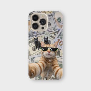 May include: A phone case featuring a selfie of a ginger cat wearing pixelated sunglasses, with two black kittens and a background of US hundred-dollar bills. The case has a glossy finish and a camera cutout.