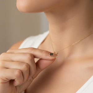 May include: A gold-colored necklace featuring a pendant shaped like the United States, with the American flag design. The pendant is small and detailed, with red, white, and blue colors. The necklace is delicate and appears to be made of metal.