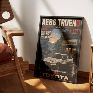 Könnte beinhalten: Ein gerahmtes Poster mit einem weißen AE86 Trueno Auto vor einem Geschäft mit japanischem Text. Das Design enthält den Text AE86 TRUENO, 1986, TOUGE, LIGHTWEIGHT, DRIFT ICON, PURE BALANCE, MASTER THE DOWNHILL, BORN FOR THE MOUNTAINS und TOYOTA.