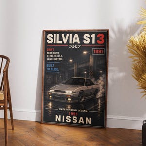 Op de afbeelding: Een ingelijste poster met een zilveren Nissan Silvia S13 auto met rook. De poster bevat de tekst "SILVIA S13" en "NISSAN", samen met Japanse karakters. Andere tekstelementen zijn "DRIFT", "REAR DRIVE" en "1991".