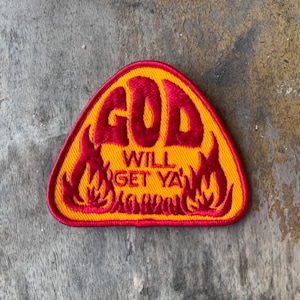 May include: A triangular embroidered patch with a yellow background and a red border. The patch features the red embroidered text GOD WILL GET YA, surrounded by red flame-like designs on the left and right sides of the lettering.