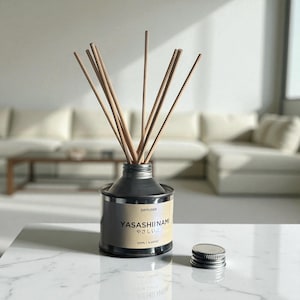 Könnte beinhalten: Ein silber-schwarzer Diffusor mit Holzstäbchen. Auf dem Etikett steht "YASASHII NAMI" und "やさしい波". Der Diffusor hat 125 ml / 4,22 fl oz. Ein silberner Deckel liegt neben dem Diffusor auf einer weißen Oberfläche.